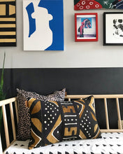 Load image into Gallery viewer, Brown, black, and white mudcloth pillows with geometric designs styled on Scandinavian bench. Modern pillows made in USA, designed in Mali. Seen here with African art.
