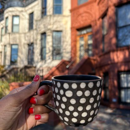 Handmade ceramic mug in minimalist dots design set against a backdrop of brownstones in Brooklyn.