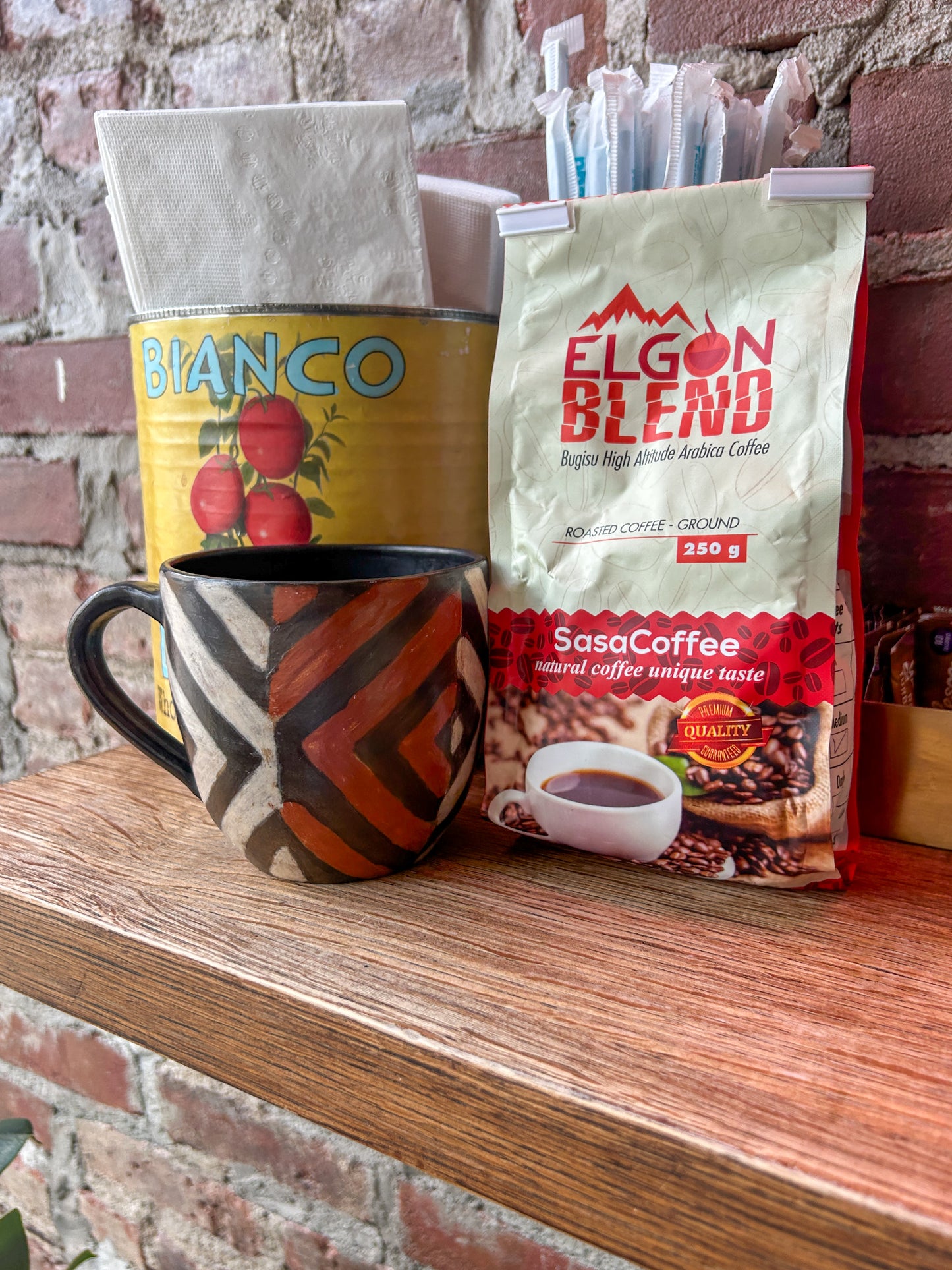 Coffee mug and bags of Ugandan Sasa coffee on a wooden surface with a brick wall background