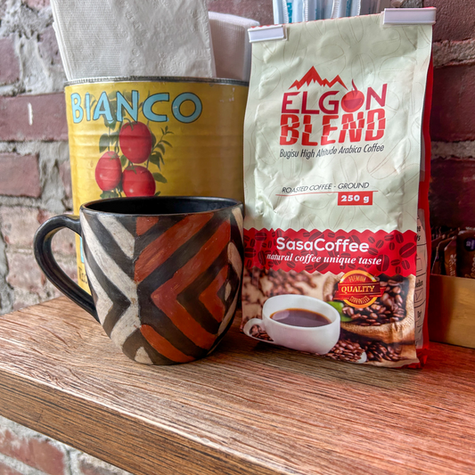 Coffee mug and bags of Ugandan coffee on a wooden surface with a brick wall background in a Brooklyn cafe.