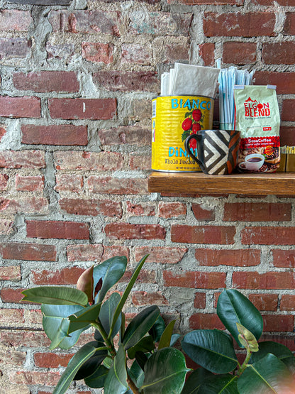 Brick wall with a shelf holding Ugandan coffee, ceramics, and a plant in the foreground.