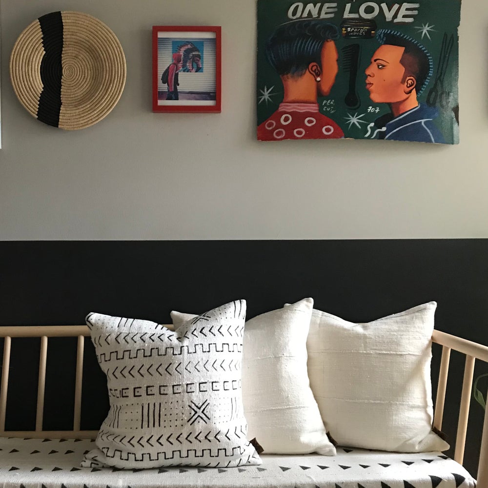 Handcrafted African mudlcoth pillow in minimalist white for modern homes. Seen with African art and baskets on stylish bench.