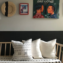 Load image into Gallery viewer, Handcrafted African mudlcoth pillow in minimalist white for modern homes. Seen with African art and baskets on stylish bench.
