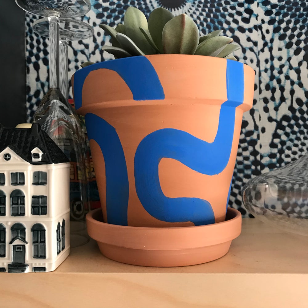 Handpainted terracotta planters with Bauhaus bohemian painted designed in blue. Perfect housewarming gift for herbs, succulents, and indoor house plants. African textile wallpaper in the background with open shelving.