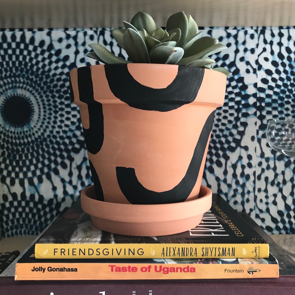 Handpainted terracotta planters with Bauhaus bohemian painted designed. Seen here in black. Perfect housewarming gift for herbs, succulents, and indoor house plants. African textile wallpaper in the background with open shelving.