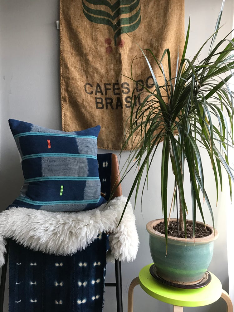 Blue Handcrafted vintage Baule pillow with accent embroidery. Ivory Coast textile and African home goods. On a modern bench with indigo tablerunner and sheepskin; global art in the background.