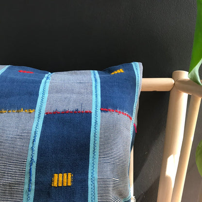 Blue Handcrafted vintage Baule pillow with accent embroidery. Ivory Coast textile and African home goods. On a modern bench with mudcloth runner on the table and African art in the background.