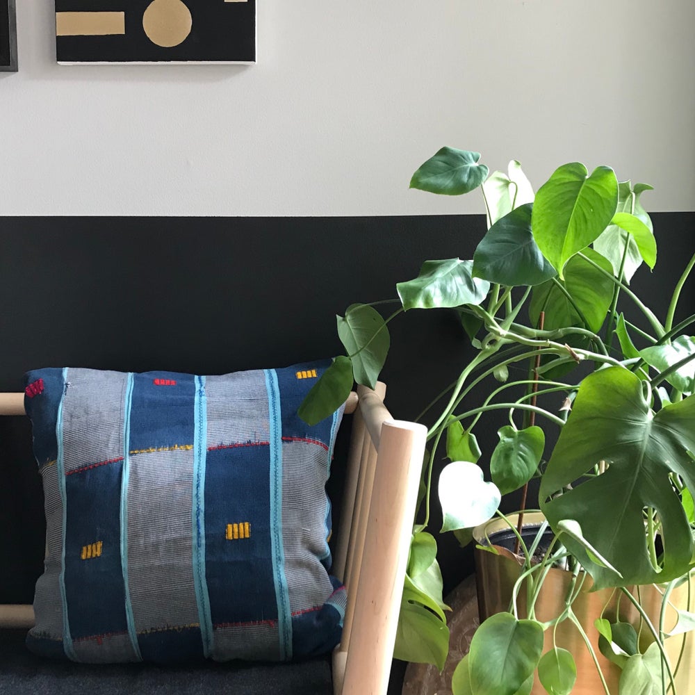 Blue Handcrafted vintage Baule pillow with accent embroidery. Ivory Coast textile and African home goods. On a modern bench with mudcloth runner on the table and African art in the background.