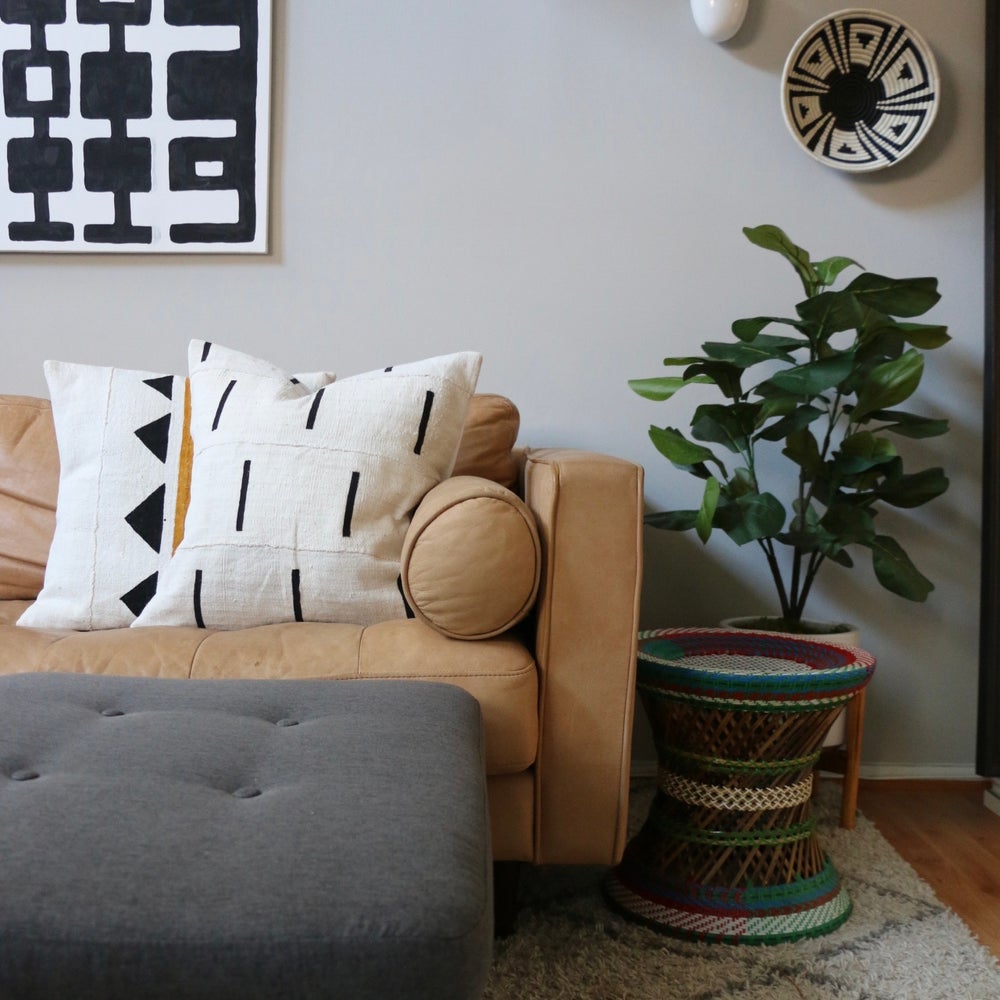 Handcrafted African mudcloth pillow in minimalist white for modern homes. Black and white seen here with African basket on leather sofa.