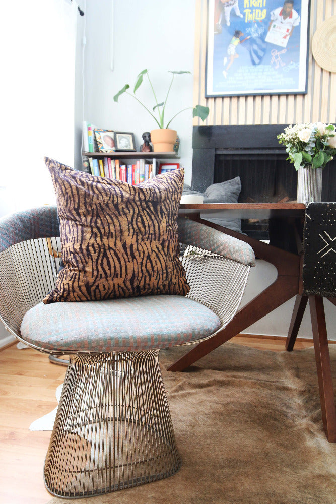 Batik and mudcloth textile home goods in modern Boho home, pillows made in Tanzania on Platner chair. African art and monstera plant.